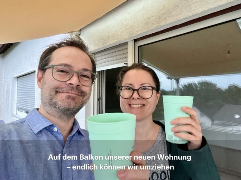 Andrea und ihr Partner stehen lachend auf dem Balkon ihrer neuen Wohnung und prosten mit ReCup-Bechern in die Kamera.