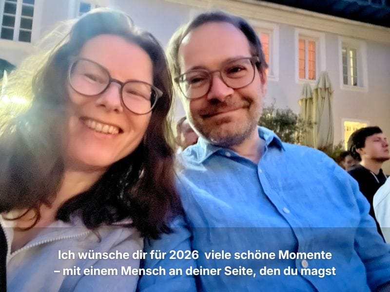Andrea und ihr Partner sitzen draußen und lächeln in die Kamera, hinter ihnen leuchtet ein Licht.